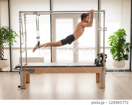 A man performs aerial exercises on a reformer machine. 128965772