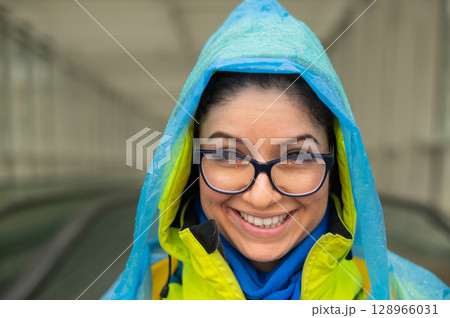 Portrait of a smiling woman with glasses wearing a raincoat outdoors. Portrait of a smiling woman with glasses wearing a raincoat outdoors. 128966031