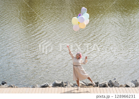 A woman with colored hair and an armful of balloons walks along the river embankment. 128966231