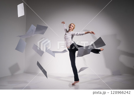 A graceful ballerina in a business suit throws documents. Business woman dance barefoot on a white background A graceful ballerina in a business suit throws documents. Business woman dance barefoot on a white background 128966242