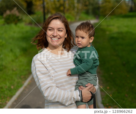 Caucasian woman holds her one-year-old son in her arms while walking in the park in autumn.  128966262