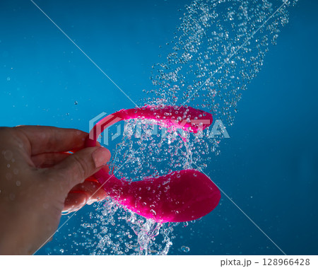 Woman washing pink curved vibrator in shower. Waterproof sex toy on blue background. 128966428