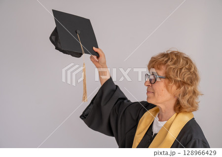 An elderly woman holds a graduation hat. An elderly woman holds a graduation hat. 128966429