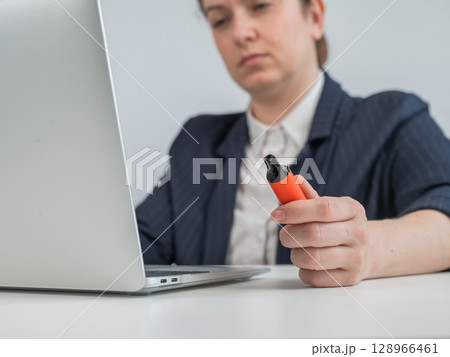 Caucasian businesswoman smokes disposable vape and works on laptop. Caucasian businesswoman smokes disposable vape and works on laptop. 128966461