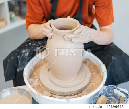 Close-up of a potter's hands making a ceramic vase on a potter's wheel. Close-up of a potter's hands making a ceramic vase on a potter's wheel. 128966484