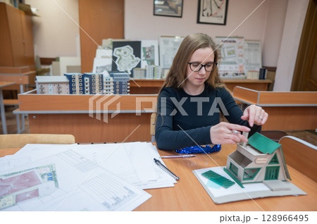 Caucasian young woman making a model of a building. Student of the construction university. Caucasian young woman making a model of a building. Student of the construction university. 128966495
