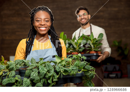 Two colleagues holding pots of plants in the flower shop and looking contented and enjoyed 128966686
