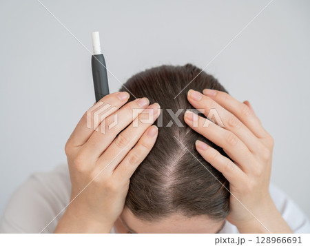 Tired woman smoking an electronic cigarette while working on a laptop. Tobacco heating system. 128966691