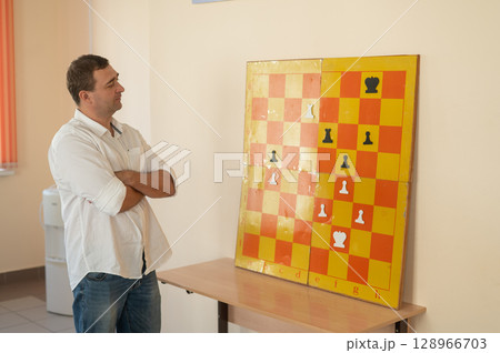 Caucasian man standing at wall mounted magnetic chessboard demonstration.  128966703