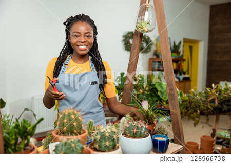 Flower shop assistant cutting flowers and looking contented and happy Flower shop assistant cutting flowers and looking contented and happy 128966738