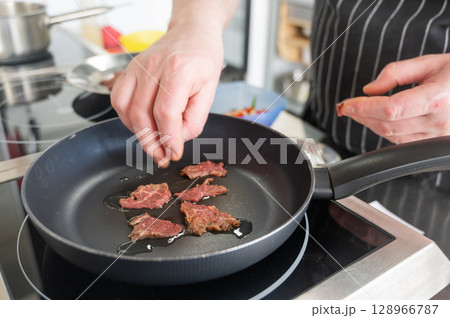 The chef fries veal in a frying pan.  128966787