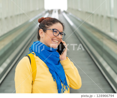 Happy woman stands on a travelator and talks on a cell phone Happy woman stands on a travelator and talks on a cell phone 128966794