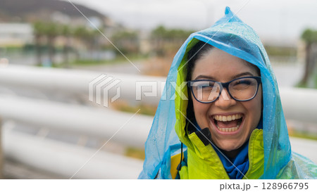 Portrait of a smiling woman with glasses wearing a raincoat outdoors. Portrait of a smiling woman with glasses wearing a raincoat outdoors. 128966795