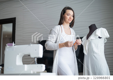 Caucasian woman sews a dress at home. Workspace of a seamstress 128966801