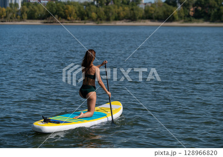 Caucasian woman riding a SUP board on the lake. Summer sport. 128966820