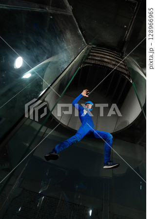 A man in overalls and a protective helmet enjoys flying in a wind tunnel. Free fall simulator A man in overalls and a protective helmet enjoys flying in a wind tunnel. Free fall simulator 128966965