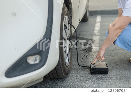 A woman pumps up a tire on a car. A woman pumps up a tire on a car. 128967084
