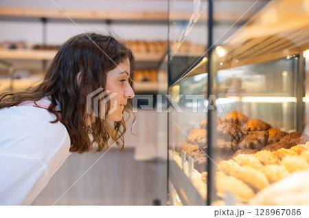 Caucasian woman looks greedily at baked goods in a bakery.  128967086