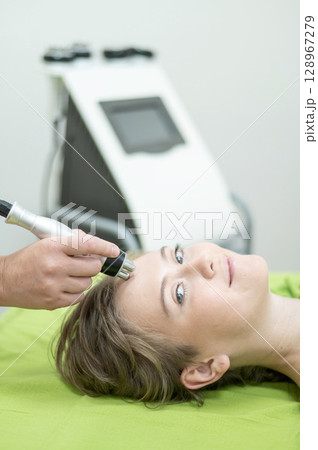 Caucasian woman undergoing radio wave RF lifting procedure in beauty salon. Caucasian woman undergoing radio wave RF lifting procedure in beauty salon. 128967279