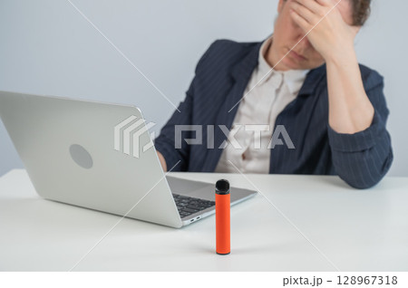 Caucasian businesswoman working on laptop. Disposable vape in foreground.  128967318