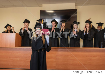 Happy Caucasian woman holds red diploma and classmates support her. Happy Caucasian woman holds red diploma and classmates support her. 128967324