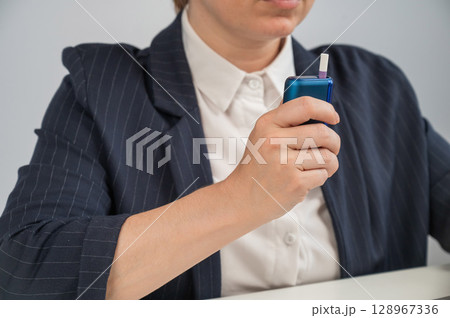 Business woman smoking an electronic cigarette while working on a laptop. Tobacco heating system. Business woman smoking an electronic cigarette while working on a laptop. Tobacco heating system. 128967336