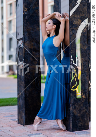 Beautiful asian ballerina in blue dress and pointe shoes posing outdoors. Vertical photo.  128967380