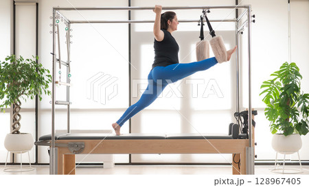 Focused Woman Practicing Pilates on a Reformer. Focused Woman Practicing Pilates on a Reformer. 128967405