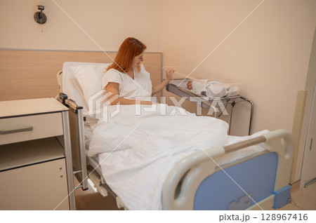 A young mother admires her newborn son in the maternity hospital. A young mother admires her newborn son in the maternity hospital. 128967416