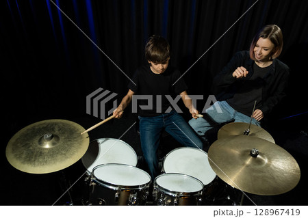 Young caucasian woman teaches a boy to play the drums in the studio on a black background. Music school student 128967419