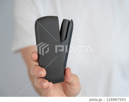 A woman takes a tobacco heating system out of a charger. Electronic cigarette. A woman takes a tobacco heating system out of a charger. Electronic cigarette. 128967503