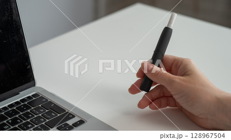 A woman smokes an electronic cigarette while working on a laptop. Tobacco heating system. A woman smokes an electronic cigarette while working on a laptop. Tobacco heating system. 128967504