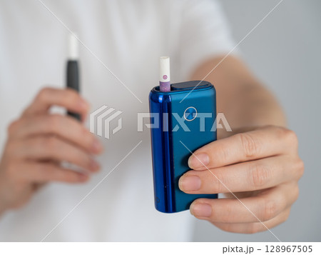 A woman compares two different tobacco heating systems. Electronic cigarette. 128967505