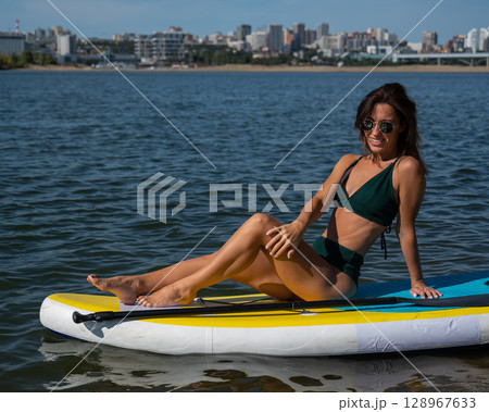 Beautiful caucasian woman is swimming on a SUP board. Beautiful caucasian woman is swimming on a SUP board. 128967633