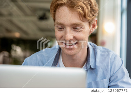 Young smiling man sitting at the table in a cafe and having a video call Young smiling man sitting at the table in a cafe and having a video call 128967771