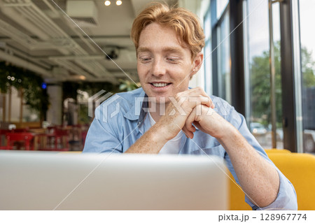 Young smiling man sitting at the table in a cafe and having a video call 128967774