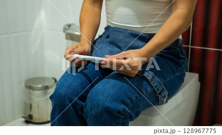 A woman takes an express pregnancy test while sitting on the toilet. 128967775