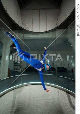 A man in overalls and a protective helmet enjoys flying in a wind tunnel. Free fall simulator A man in overalls and a protective helmet enjoys flying in a wind tunnel. Free fall simulator 128967785