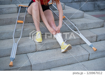 Girl with leg injury sits on the stairs with crutches. Girl with leg injury sits on the stairs with crutches. 128967812