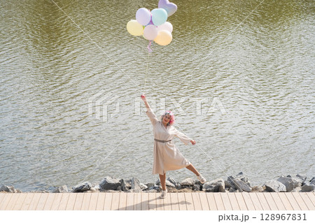 A woman with colored hair and an armful of balloons walks along the river embankment. 128967831