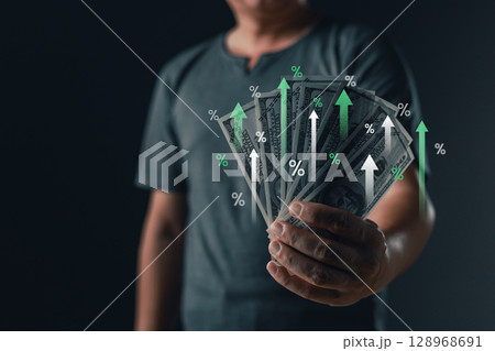 A person holds a fan of US dollar bills with digital percentage symbols and upward arrows, representing financial growth, investment success, and economic gain. profit and wealth increase. 128968691