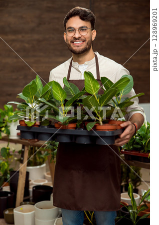 Smiling young man in eyeglasses holding flower pots and looking enjoyed 128969201