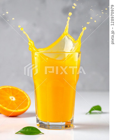 Orange Juice Splashing in Glass with Halved Orange and Green Leaves Still Life 128970979