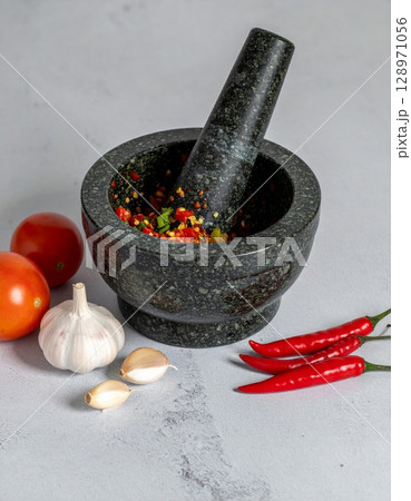 Granite Mortar and Pestle with Chillies Garlic and Tomatoes on Gray Surface Still Life 128971056