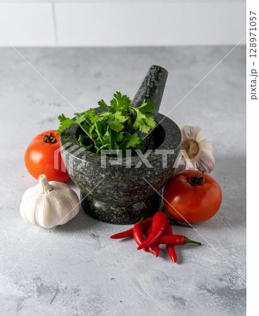 Close Up of Stone Mortar and Pestle Surrounded by Fresh Red and Green Produce 128971057