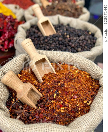 Burlap Sacks Filled with Red Crushed Chili and Black Pepper with Wooden Spoons 128971449