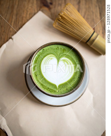 Matcha Latte with Heart Foam Art and Bamboo Whisk on Wooden Table Background 128971528