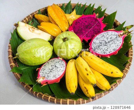 Vibrant Assortment of Fresh Tropical Fruits on Woven Basket Plate with Banana Leaf Vibrant Assortment of Fresh Tropical Fruits on Woven Basket Plate with Banana Leaf 128971646