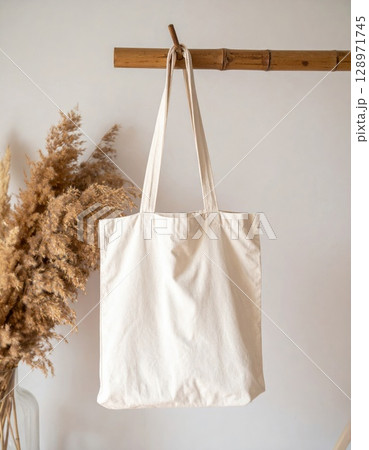 Beige Cotton Canvas Tote Bag Mockup Hanging on a Wooden Rack with Pampas Grass 128971745