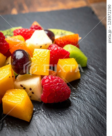 Colorful Fruit Salad with Mango Kiwi Berries and Grapes on Black Slate Backdrop 128972290